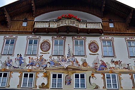 Oberbayern - Munteres Treiben: Feiergesellschaft am Geburtshaus des Schriftstellers Ludwig Thoma in Oberammergau. Die Figuren porträtieren die damaligen Bewohner (Malerei von 1969)