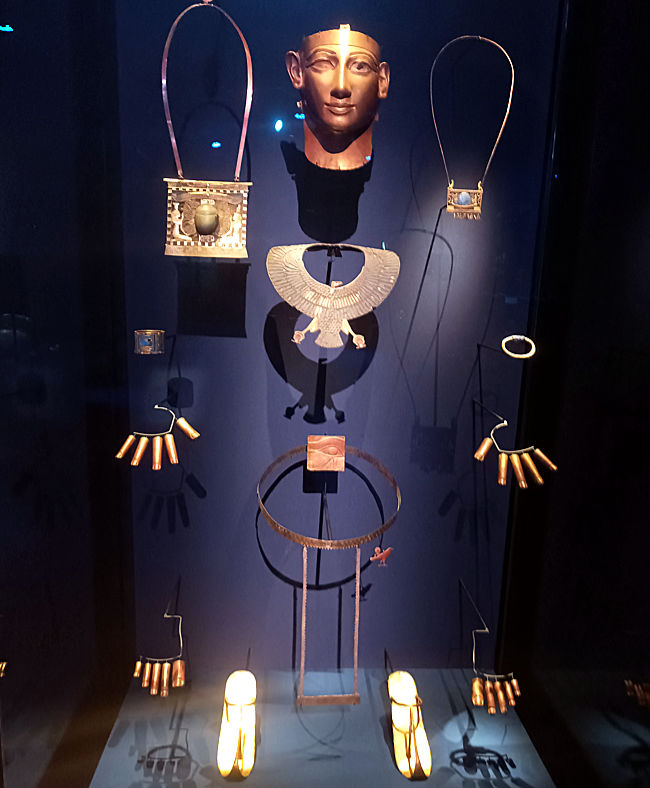 Odysseum, Ausstellung, Mumien-Schmuck von Scheschonk II., 22. Dynastie. Die Mumie war mit einer goldenen Totenmaske, Amuletten, einem Gürtel, Schmuck und goldenen Fingerlingen und Zehfingerlingen geschmückt, die ihn zu einem strahlenden, leuchtenden Wesen machten. Viele weitere Amulette – alle mit Bedeutung und magischen Kräften versehen, die Unsterblichkeit verleihen – wurden auf die Mumie und zwischen die Lagen von Bandagen gelegt, die sie umhüllen. Einige gehörten früheren Königen, andere kamen aus fernen Ländern.