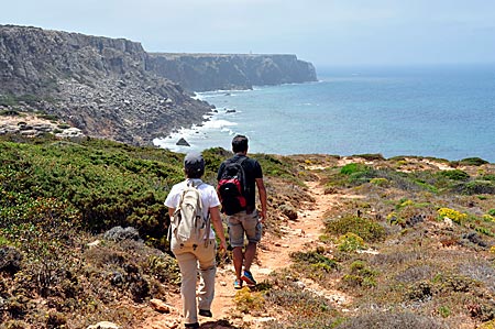 Wanderer auf der Rota Vicentina im Naturpark Costa Vicentina, mit Blick auf den fernen Leuchtturm am Cabo de São Vicente, Algarve, Portugal