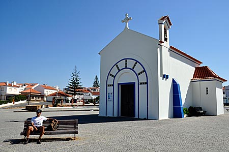 Pausierender Wanderer vor der Kapelle Nossa Senhora do Mar in Zambujeira do Mar, Etappe des Fischerweges der Rota Vicentina, dem Fernwanderweg durch den gleichnamigen Naturpark im Südwesten Portugals
