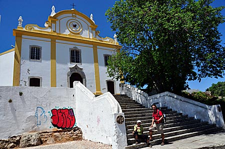 Wanderer vor der Kirche in der mittelalterlichen Burg von Santiago do Cacém, Start- oder Endpunkt des Fernwanderweges Rota Vicentina durch den gleichnamigen Naturpark im Südwesten Portugals